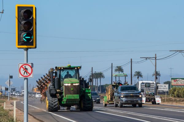Image of a large agriculture truck on State Route 166 in traffic and a no pedestrian crossing sign posted on a stoplight.