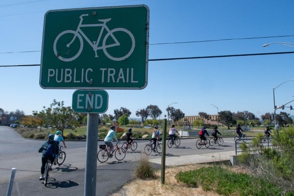 Image depicts a trail end sign in Santa Maria with a group of bicyclists in the background