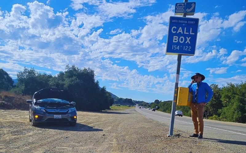 Depicts motorist with van hood ajar and using call box