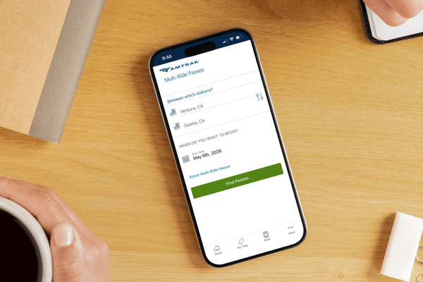 Smartphone on a desk displaying an Amtrak app screen for selecting multi-ride train passes between Ventura and Goleta.