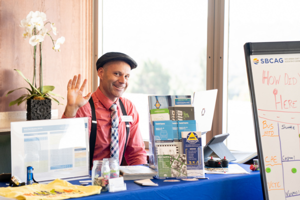 SBCAG Transportation Coordinator, Peter Williamson at an employee resources table, smiling and waving behind a display of transportation materials and information.