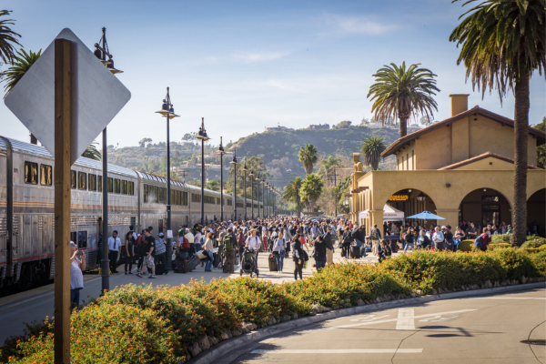 Crowd of passengers at Santa Barbara train station boarding and exiting a passenger train with palm trees and hills in the background